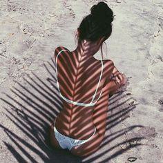 a woman sitting in the sand with her back turned to the camera and casting a shadow