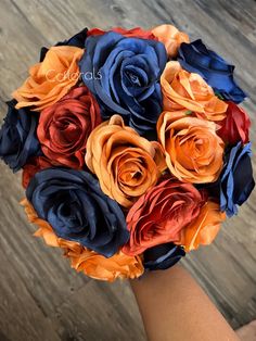 a bridal bouquet with orange, blue and red flowers is held by someone's hand