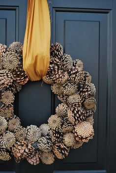 a wreath made out of pine cones is hanging on the front door with a yellow ribbon