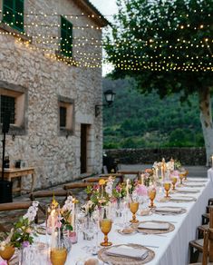 a long table is set with place settings and flowers on the table for an outdoor dinner