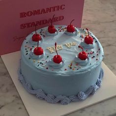 a blue cake with white frosting and cherries on top next to a card