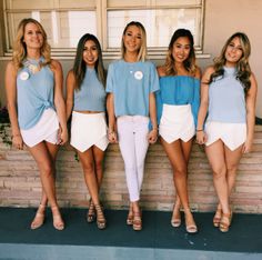 the girls are posing in front of a brick wall wearing blue tops and white shorts