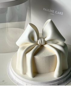 a white cake with a large bow on it's top sitting on a plate