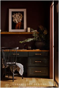 a chair sitting in front of a desk with flowers on it and a painting above the desk