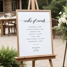 an easel with a sign that says order of events on it and flowers in the background