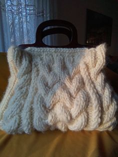 a white knitted purse sitting on top of a bed next to a window with curtains