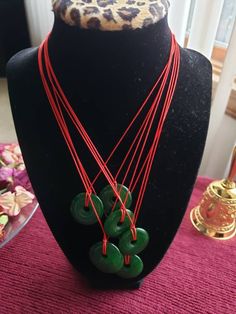 "Natural Jade donut pendant, red cord *Red Agate and Green jade beads *Different variations ~Adjustable and can be worn different ways~ *Necklace can be worn loosely or as a choker.  * When worn as a choker, back beads can be worn off to the side or in front (see photos) (A red adjuster piece will be added to the necklace if the bead that sits on the back of the neck, slides too loosely). This will allow the necklace length to hold securely in place and blend in with the red cord. *Purchases: 4 stone options available (see picture for reference) **Select your stone \"style\" choice at checkout. *Contact me if you are interested in purchasing duplicates of the same pattern, And I will do my best to accommodate based on available supplies." Adjustable Jade Necklace For Good Luck, Donut Necklace, Donut Pendant, Dangle Necklaces, Red Agate, Natural Jade, Jade Beads, Green Jade, Jade Green