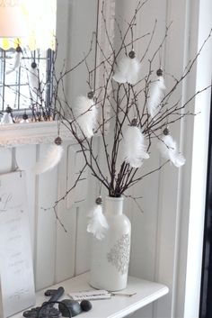 a vase with feathers and branches in it on a white shelf next to a mirror