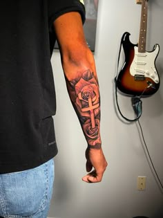 a man with a cross and rose tattoo on his arm holding an electric guitar in front of him