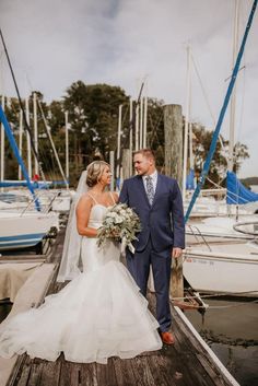 a bride and groom standing on a dock in front of sailboats at their wedding