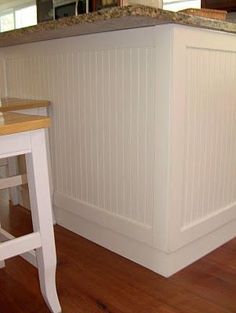 a white kitchen with an island and wooden floors in the center, along with two stools