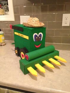 a green toy tractor with yellow blades and a straw hat on it's head