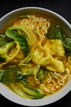 a white bowl filled with noodles, broccoli and other vegetables on top of a black surface