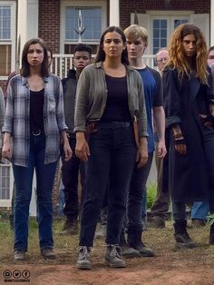 a group of people standing in front of a house with one woman looking at the camera