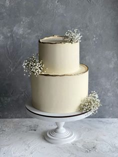 a three tiered cake with white flowers on the top and bottom is sitting on a pedestal