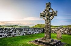 a stone cross sitting in the middle of a grassy field next to a stone wall