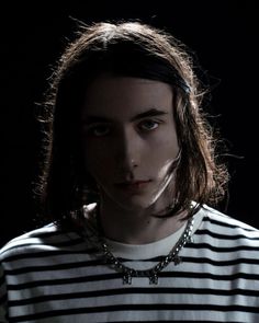 a young man with long hair wearing a striped t - shirt and silver chain necklace