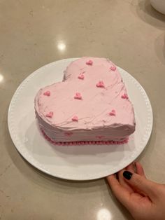 a heart shaped cake on a plate being held by a woman's hand with pink frosting