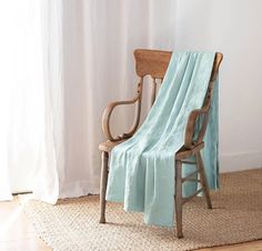 a chair with a blanket draped over it in front of a window and rug on the floor