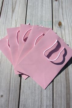 four pink paper bags sitting on top of a wooden table next to scissors and thread