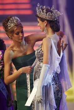 two women in evening gowns and tiaras standing next to each other