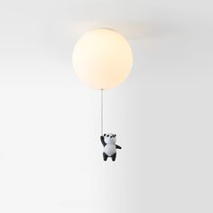 a black and white panda bear hanging from a ceiling light with a ball attached to it