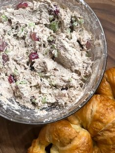 a bowl of chicken salad next to croissants on a wooden table top