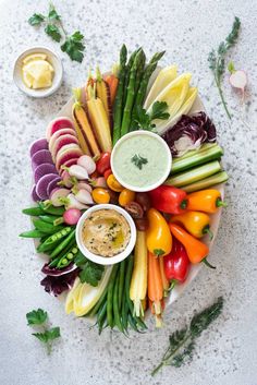 a platter filled with vegetables and dips on top of a white countertop