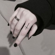 a woman's hand with a small cross tattoo on her left thumb and ring