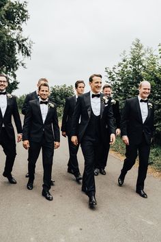 Groom and groomsmen in black tie and floral buttonholes walk down road. Black Tie Groom And Groomsmen, Wedding In Garden, Green Satin Bridesmaid, Groom Attire Black, Green Satin Bridesmaid Dresses, Sperry Tent Wedding, Black Tie Wedding Guest