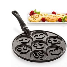 a pan with smiley faces on it next to some raspberries and pancakes in the background