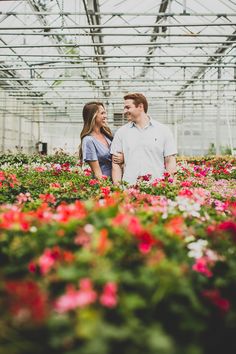 a man and woman standing in a greenhouse surrounded by pink, red and white flowers