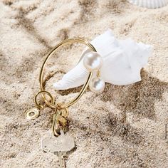 a keychain on the sand with a seashell and pearls attached to it