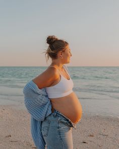 a pregnant woman standing on the beach in front of the ocean with her belly exposed