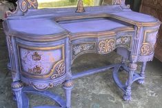 an antique desk painted in blue and gold with ornate carvings on the top, along with a mirror behind it