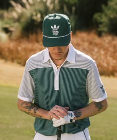 a man wearing a green hat and holding a golf club in his hands while standing on the grass