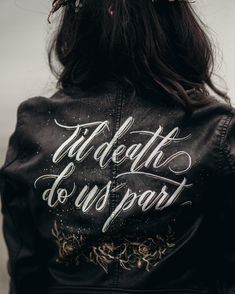 the back of a woman wearing a black leather jacket with white lettering and flowers in her hair