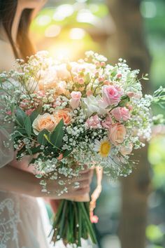 a woman holding a bouquet of pink and white flowers with greenery in the background