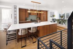 an open kitchen and dining area with wooden floors, white counter tops and bar stools