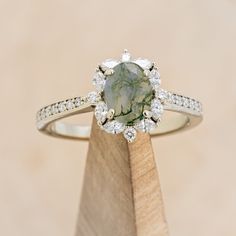 a green and white diamond ring sitting on top of a wooden stand