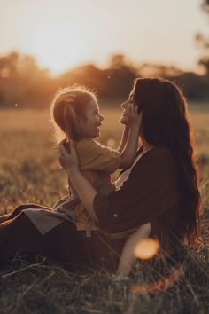 a woman sitting on the ground holding a small child in her lap and looking into the distance