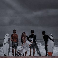 four surfers are standing on the beach with their surfboards looking out at the ocean