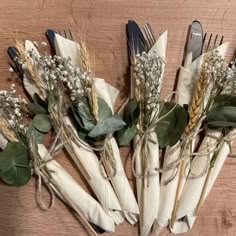 several forks and some flowers on a wooden table with white napkins tied to them