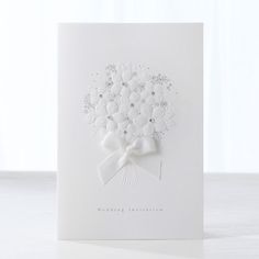 a white greeting card with a bouquet of flowers on the front and bow at the top