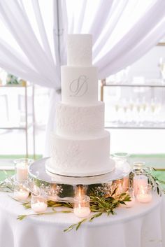 a white wedding cake sitting on top of a table covered in candles and greenery