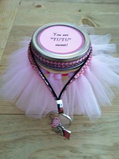 a small jar with a pink ribbon around it sitting on a wooden table next to a bottle opener