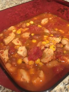 a red bowl filled with chicken, corn and tomato soup on top of a counter