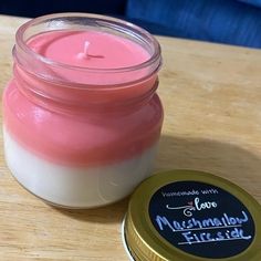 a pink and white candle sitting next to a jar of wax on top of a wooden table