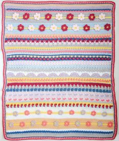 a crocheted blanket with flowers and stripes on the bottom, sitting on a white surface