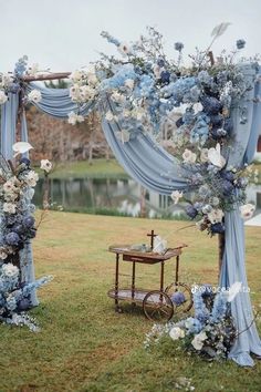 an outdoor wedding setup with blue and white flowers on the arch, chairs and table